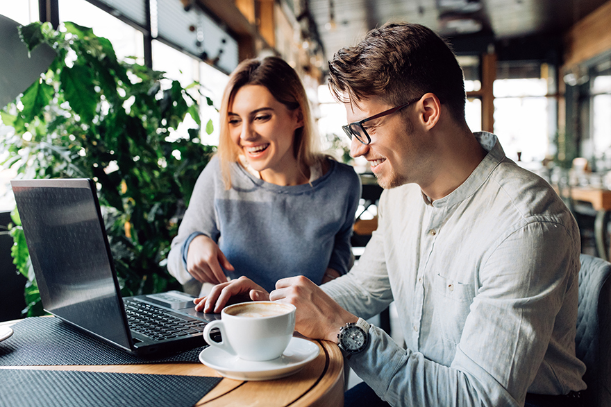 A couple sitting in a café looking at a computer laughing